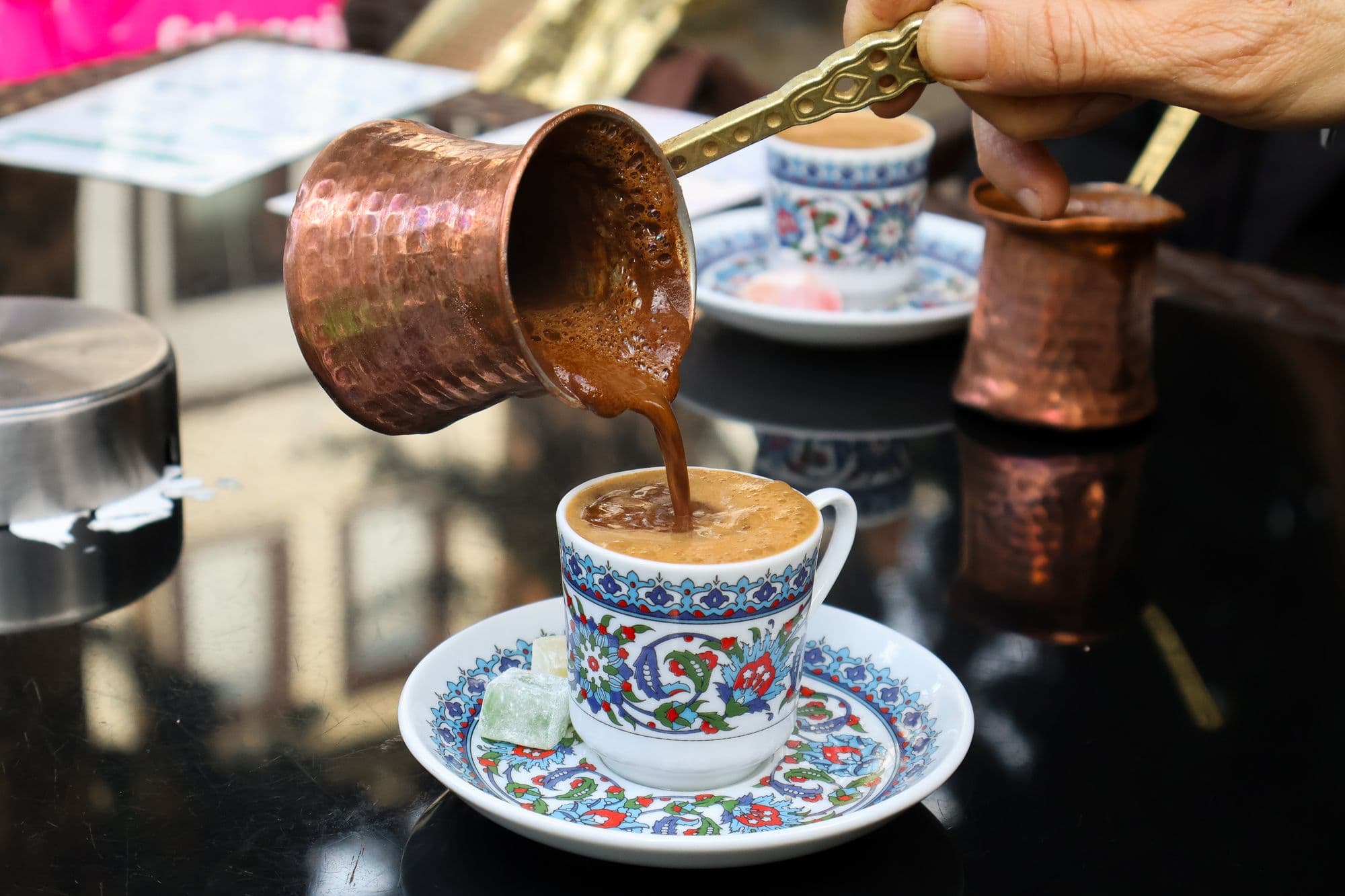 Turkish coffee poured from a copper cezve into a patterned cup