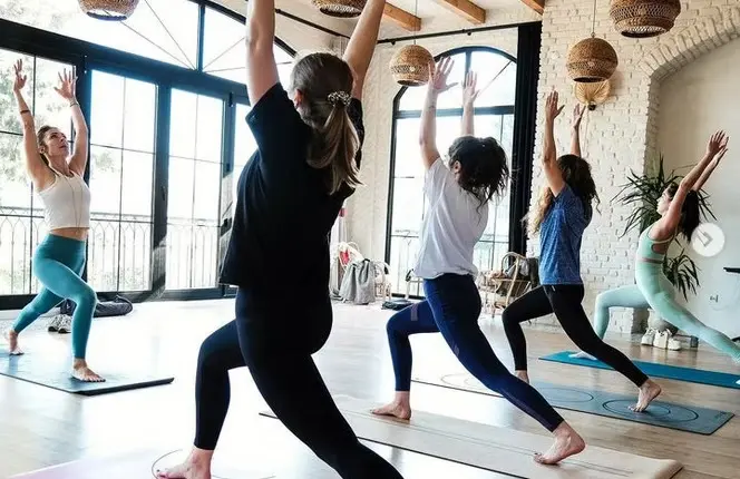 A yoga class with arms raised in the hall at Çeşmeköy, with tall arched windows
