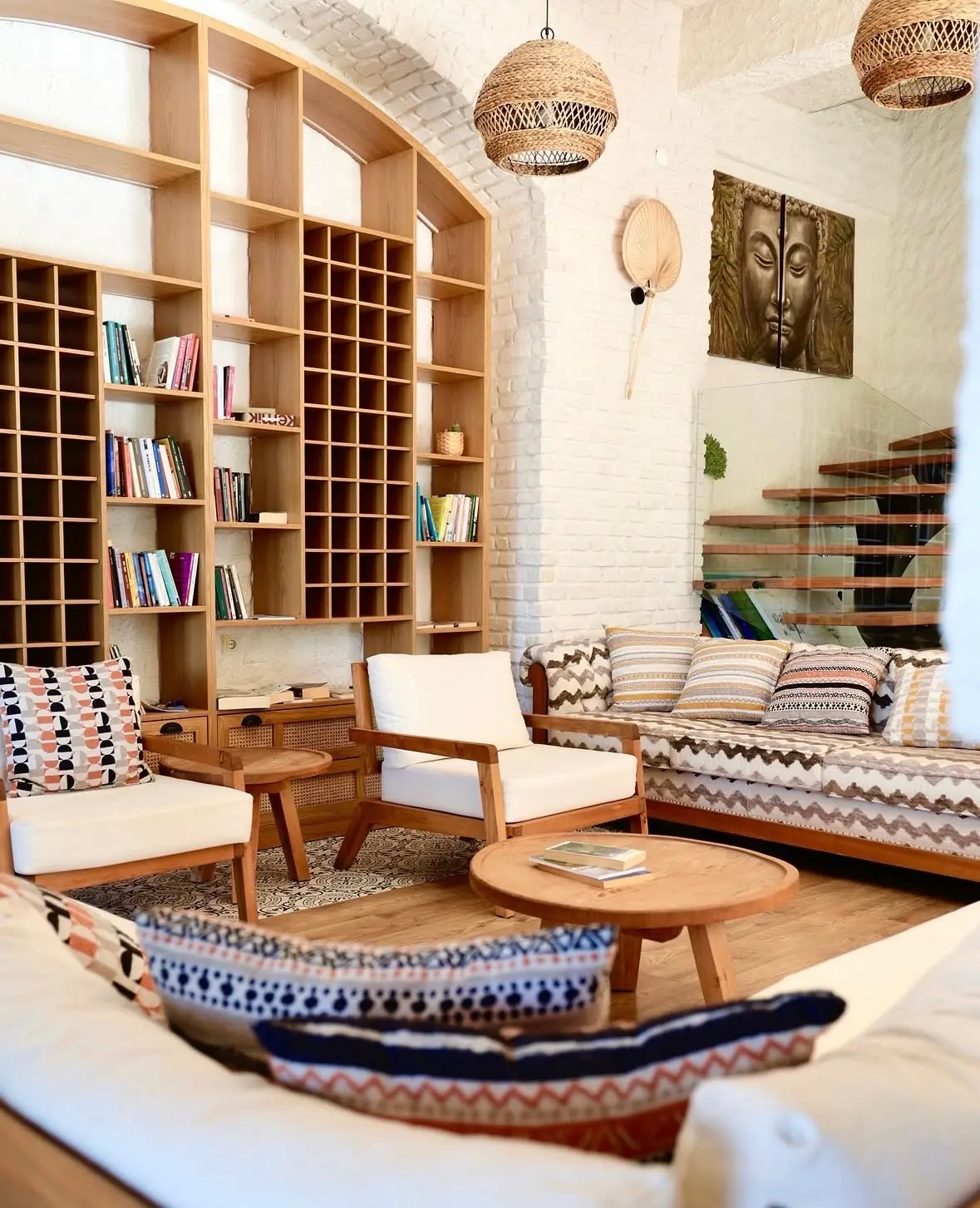Lounge at Çeşmeköy with an arched timber bookshelf, white brick walls, armchairs and patterned cushions