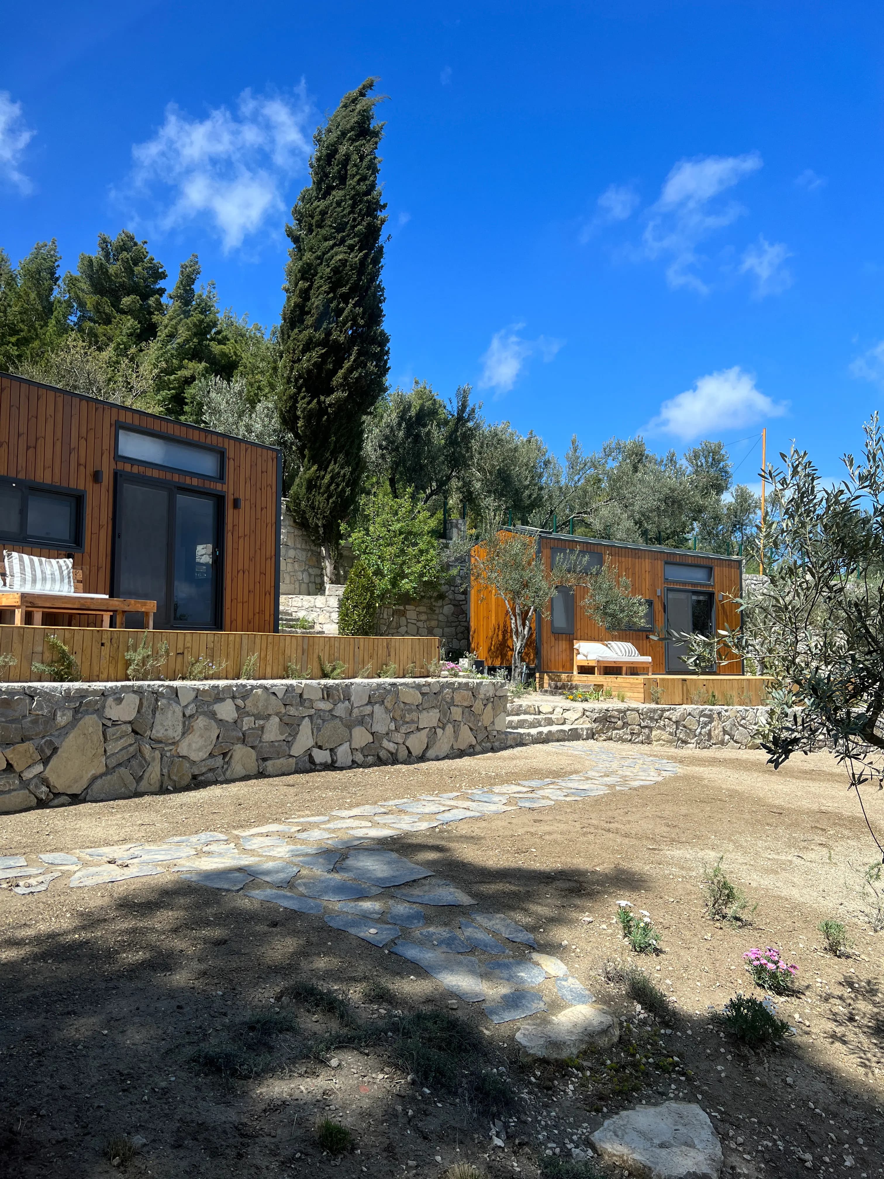 Two tiny houses with a cypress, a stone wall and stepping stones