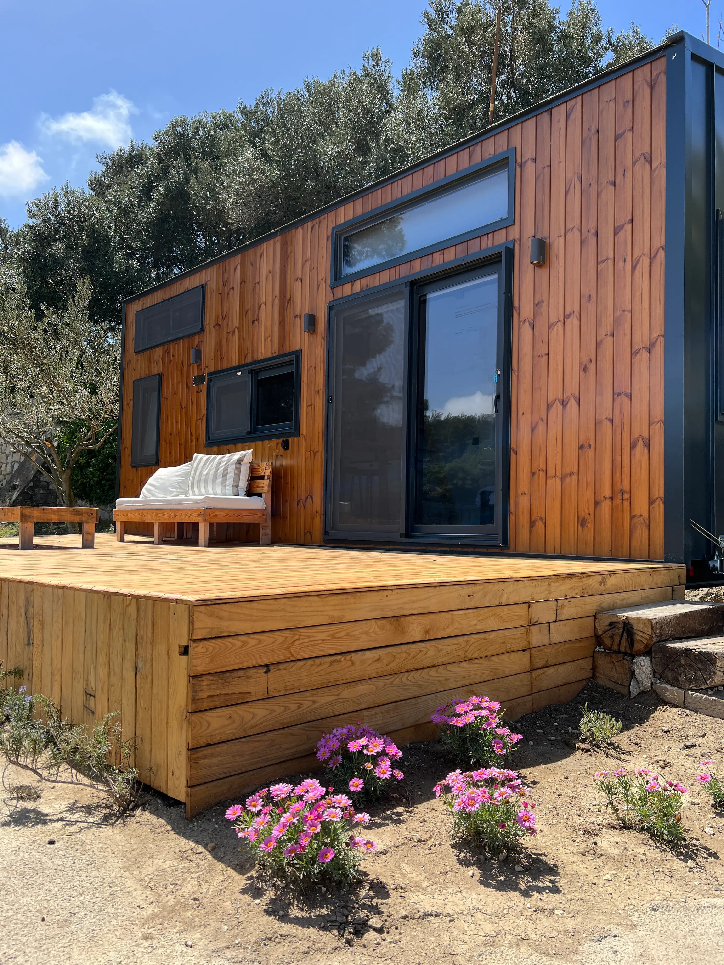 Wood clad tiny house at Çeşmeköy with a timber deck and pink flowers